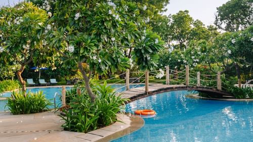 A big swimming pool with a bridge in the middle and greenery around it